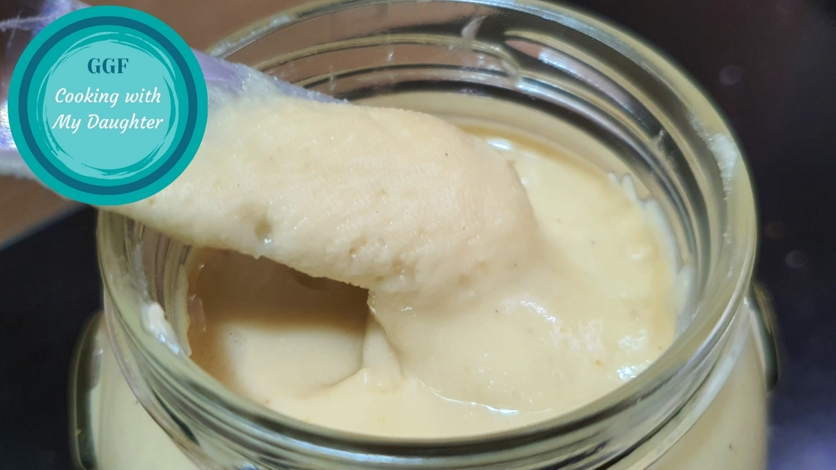Sweet cashew butter in a glass jar, seen from the top on a spreading knife