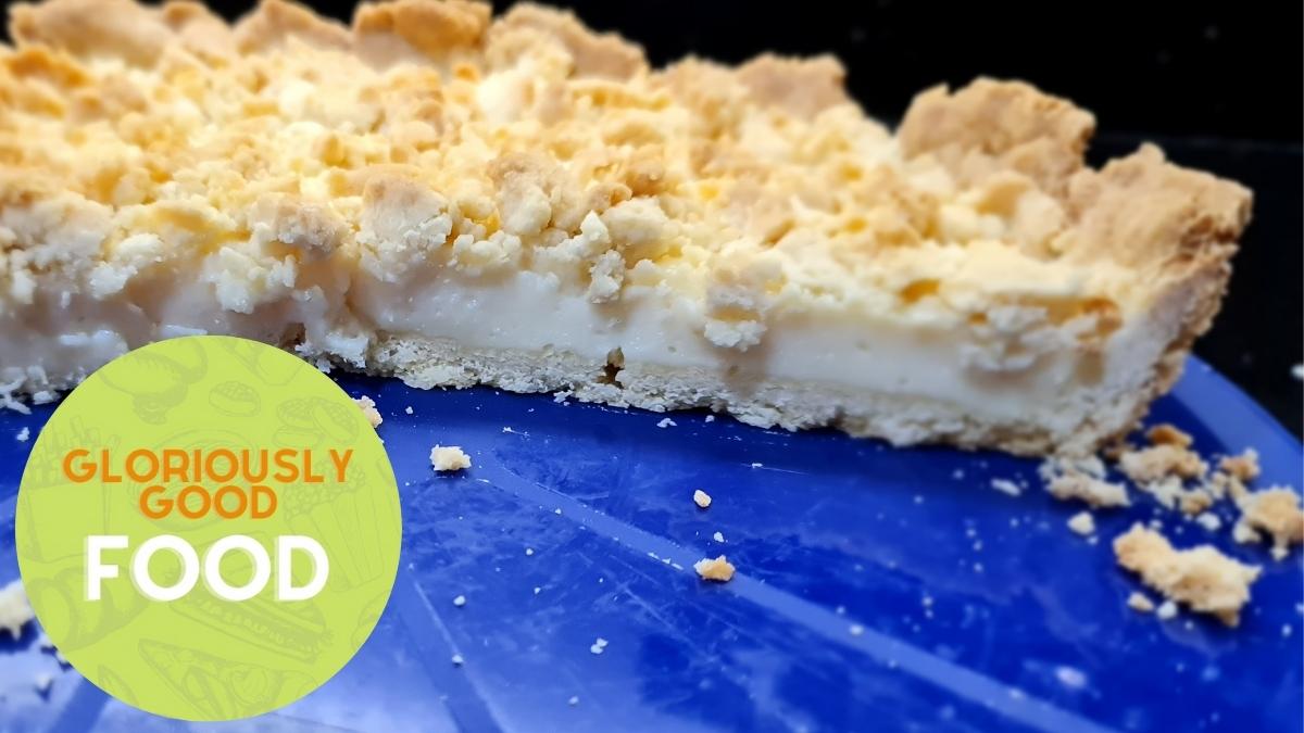 Side view of half a sliced thick custard pie with a crumble topping.